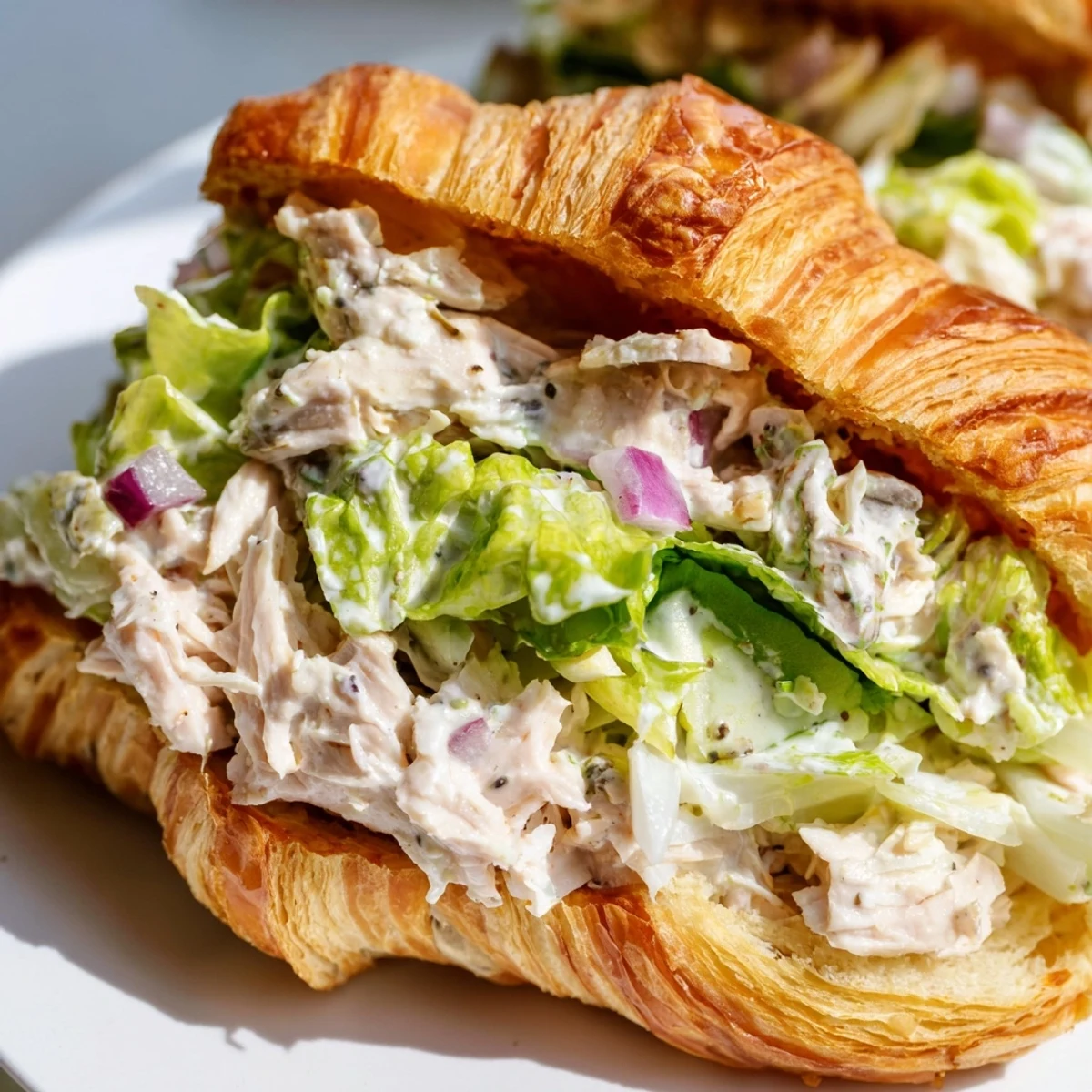 Savory chicken Caesar salad overflowing from buttery croissant with fresh lettuce and Parmesan shavings