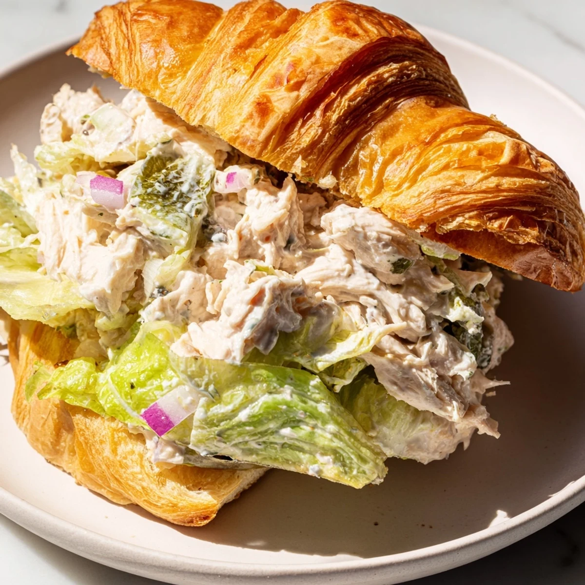 Gourmet Chicken Caesar Salad Croissant Sandwich served on plate with chopped romaine and extra cheese