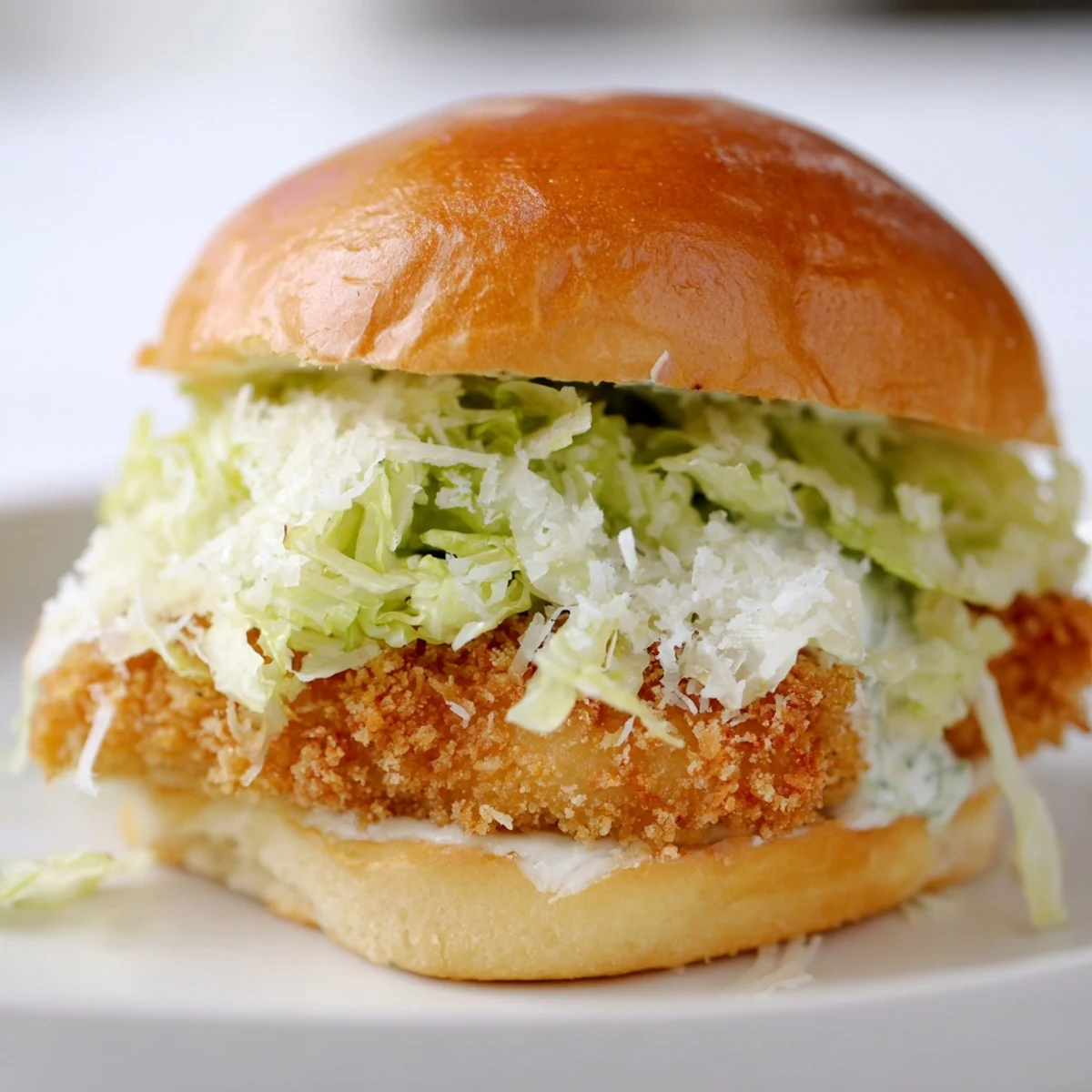 Handheld crispy chicken Caesar sandwich loaded with lettuce and creamy Caesar sauce on a warm toasted bun