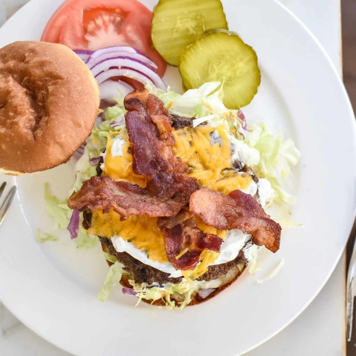 Homemade crack burger featuring cheesy beef patty topped with crunchy bacon fresh lettuce tomato and tangy crack sauce