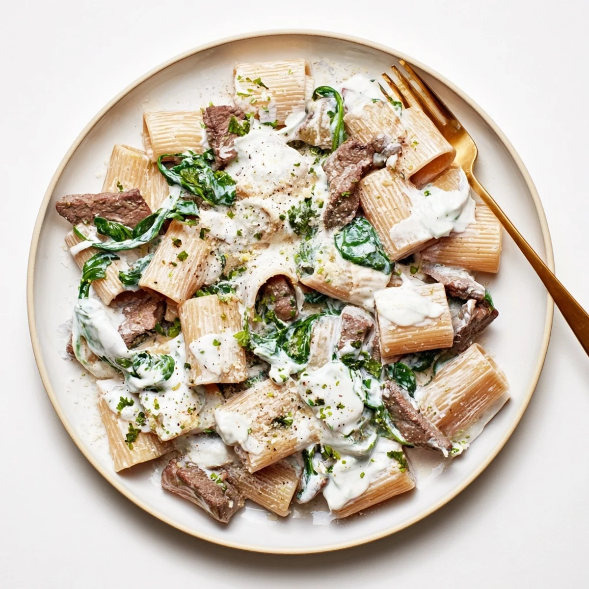 Creamy high protein beef pasta featuring tender sliced beef in a rich white sauce with wilted spinach
