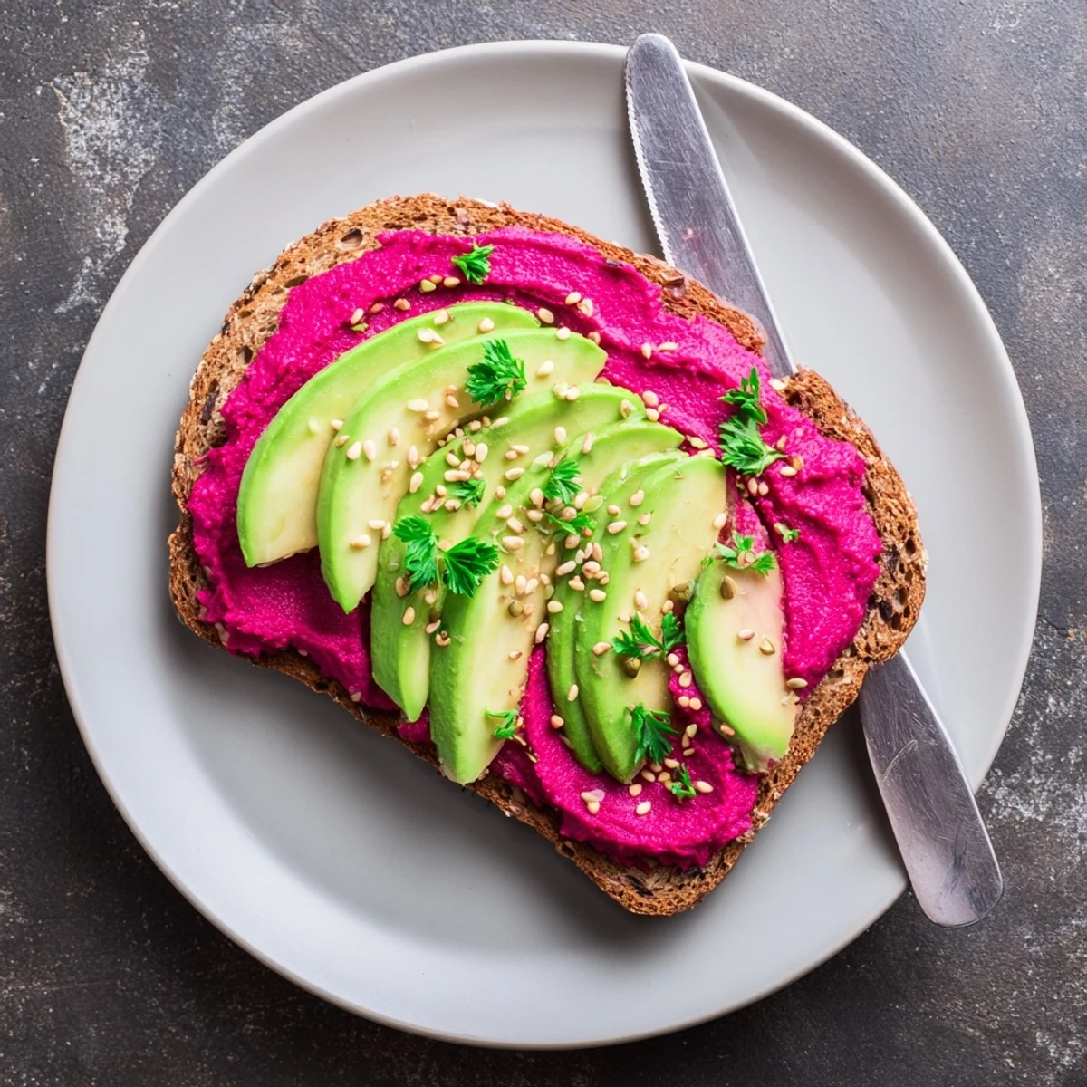 Creamy avocado and roasted beet hummus open-faced toast topped with fresh parsley and crunchy seeds