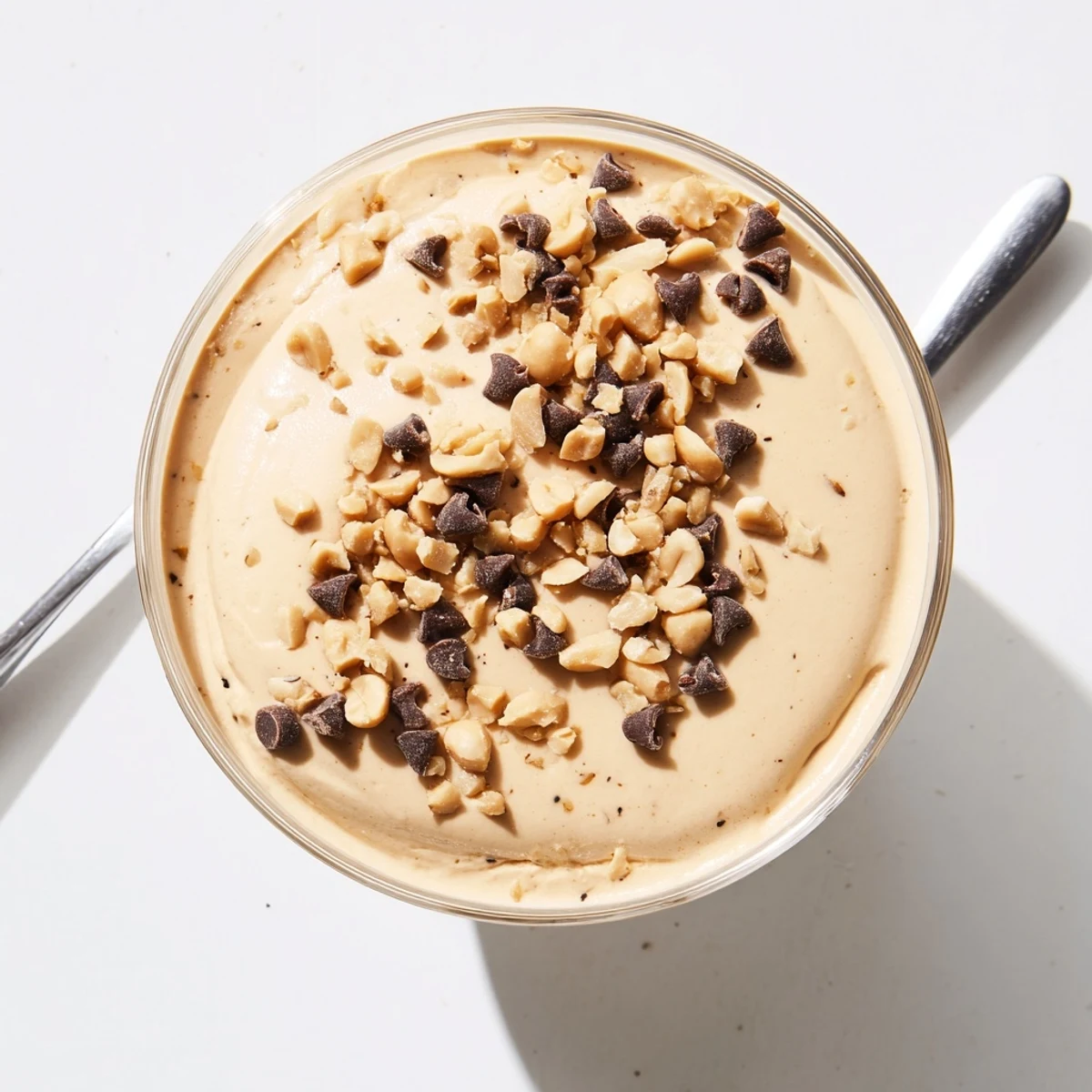 Creamy peanut butter mousse topped with chocolate chips and chopped roasted peanuts in a clear glass bowl.
