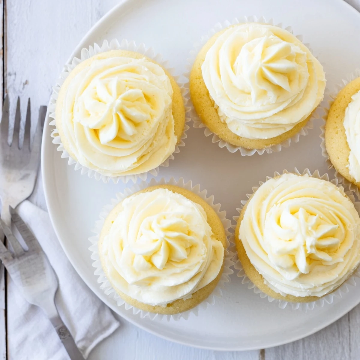 Golden vanilla cupcakes topped with fluffy white buttercream frosting on a white plate