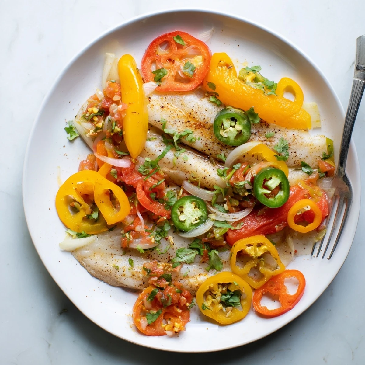 Golden tilapia fillets nestled in spicy roasted pepper skillet with vibrant red and yellow colors