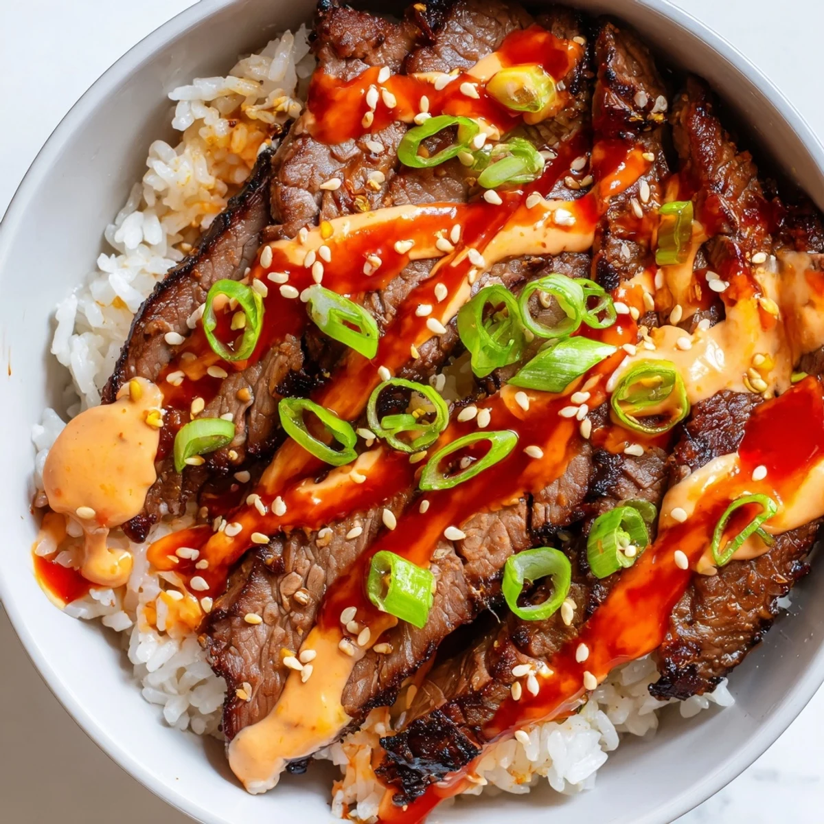Caramelized marinated steak nestled in fluffy rice with a creamy spicy drizzle
