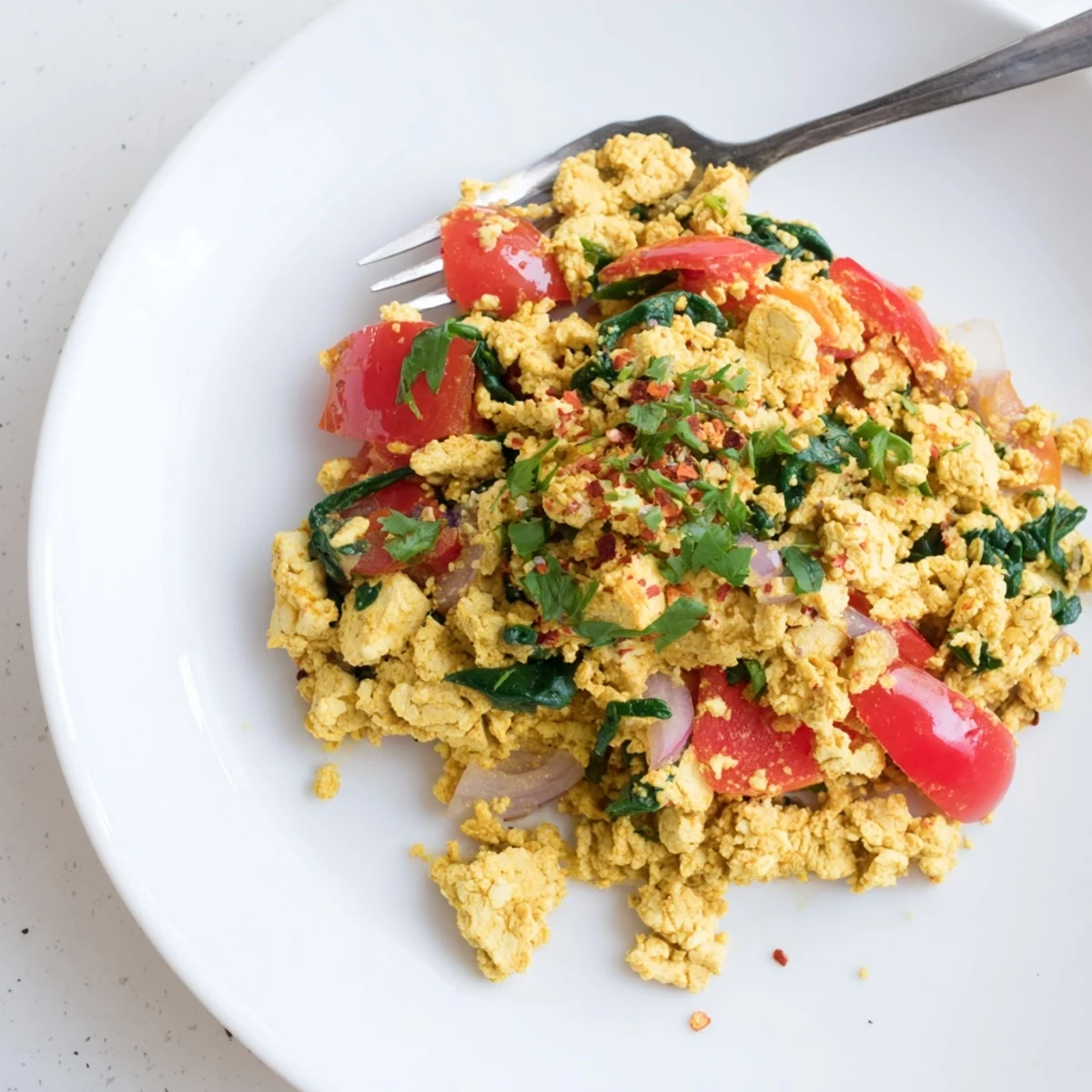 Tofu Scramble sizzling in skillet with turmeric golden crumbles and wilted spinach