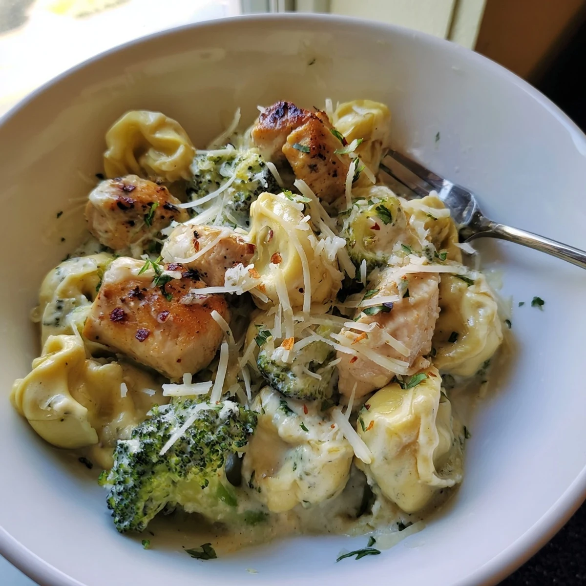 Close-up of Creamy Garlic Parmesan Tortellini Chicken Broccoli in skillet, steaming.