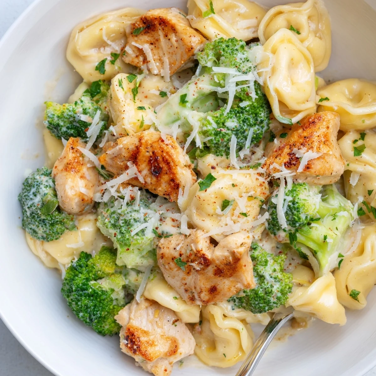 Spoon-ready Creamy Garlic Parmesan Tortellini Chicken Broccoli featuring golden seared chicken bites.