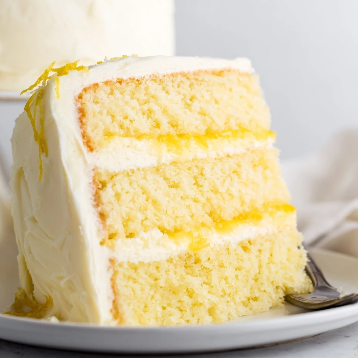 Tall lemon layer cake slice revealing zesty curd between tender yellow sponge layers