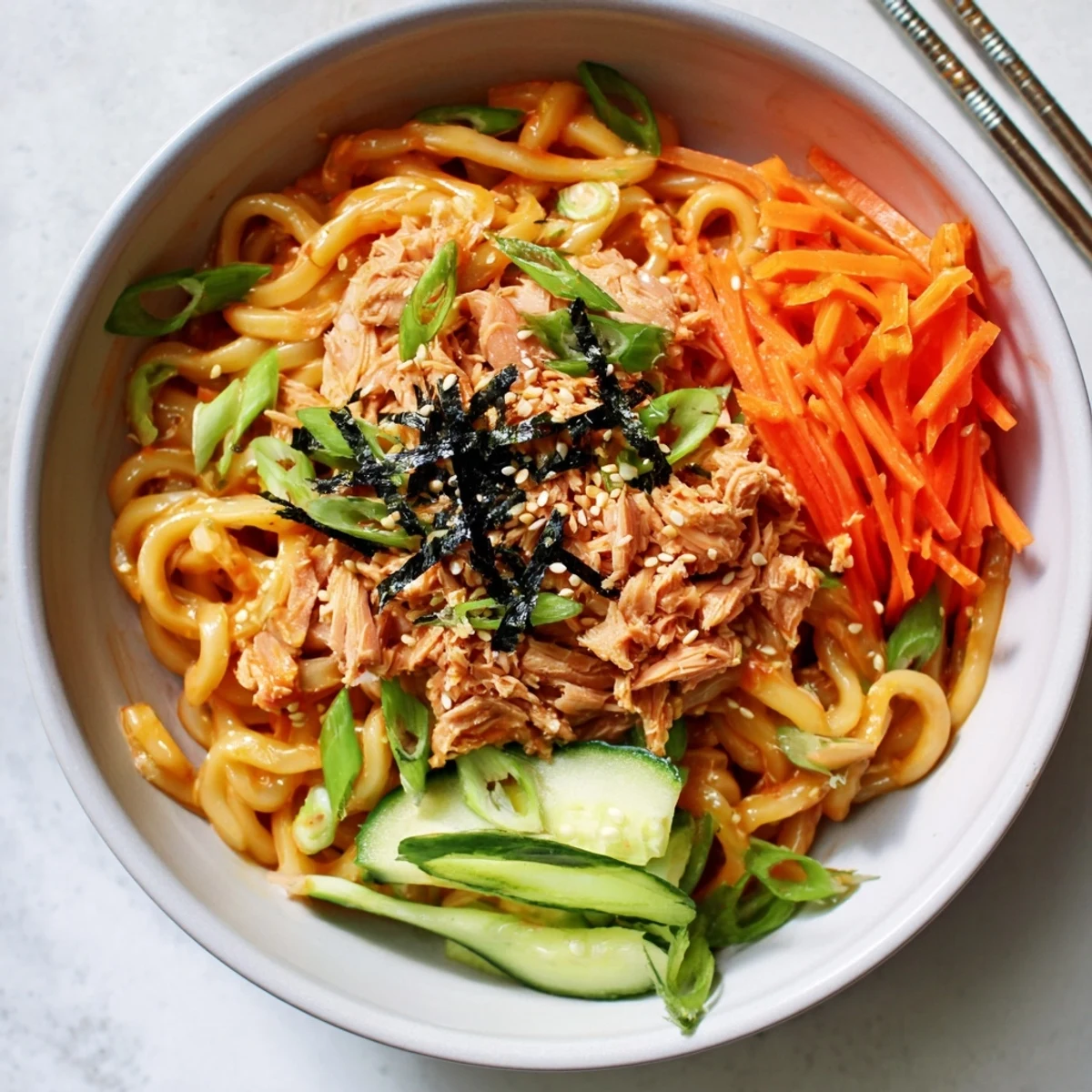 Thick udon noodles coated with spicy tuna mixture served in a wide bowl with sesame garnish
