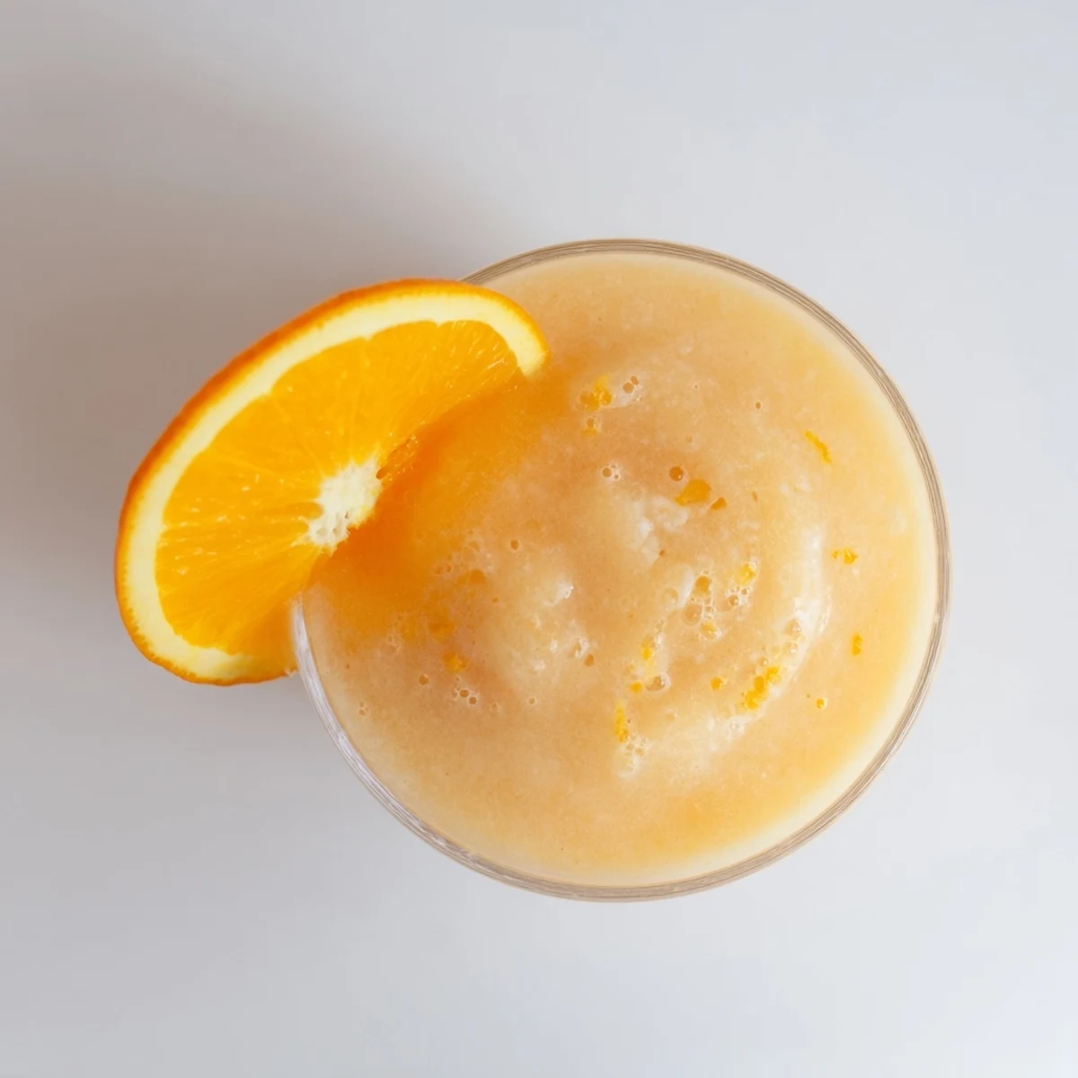 Glass of Sun Kissed Frozen Orange Cream Slush garnished with fresh orange slice on a sunny patio