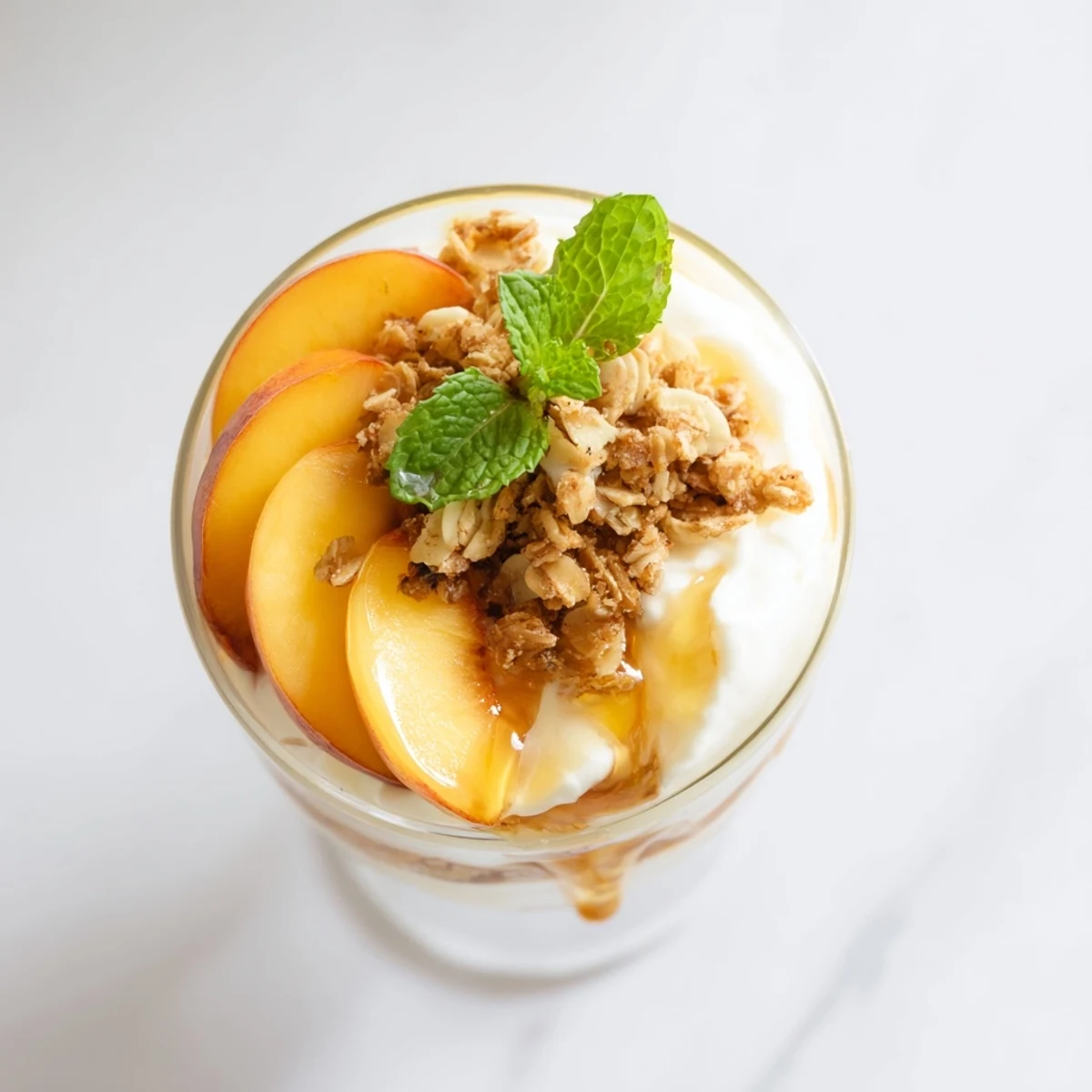 Vibrant breakfast parfait featuring ripe peach wedges layered between smooth yogurt and toasted granola with mint garnish